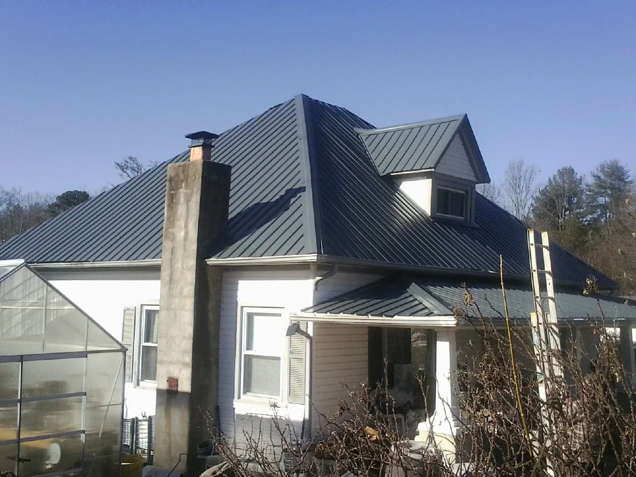 Dark blue standing seam metal roof on a white farmhouse with dormer — Slate & Tile Roof Repair by Roofing Brothers in Tuxedo Park