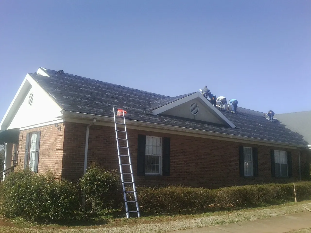 Crew tearing shingles off a brick ranch roof with a ladder set — Metal Roof Repair work by our crew in Tuxedo Park