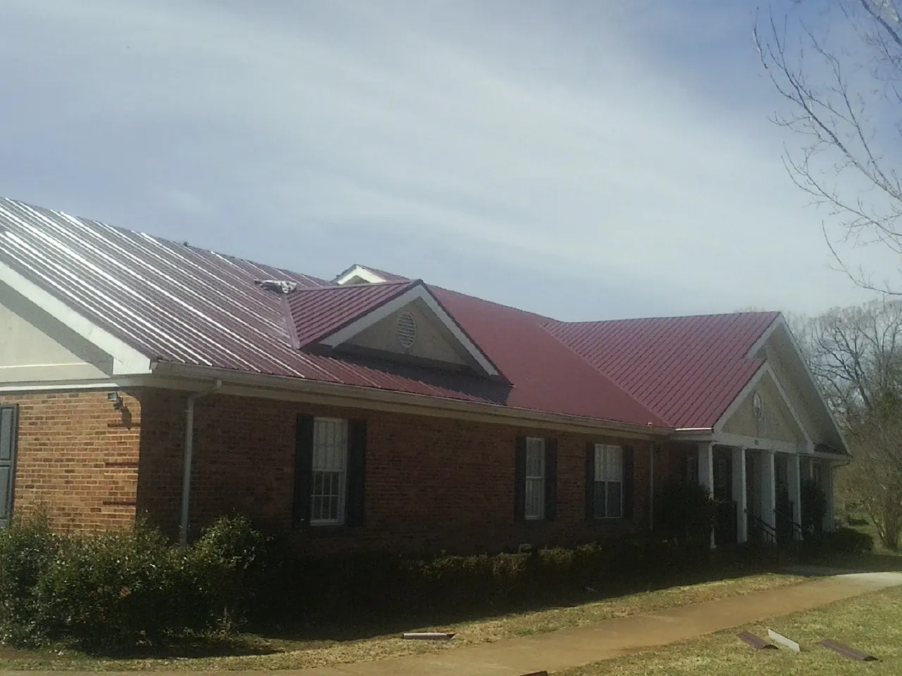 Red metal roof with gabled entries on a long brick building, from a Hail Damage Roof Repair job in Tuxedo Park
