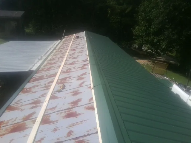 Old rusted panels beside newly installed green metal roofing — Wind Damage Roof Repair by Roofing Brothers in Tuxedo Park