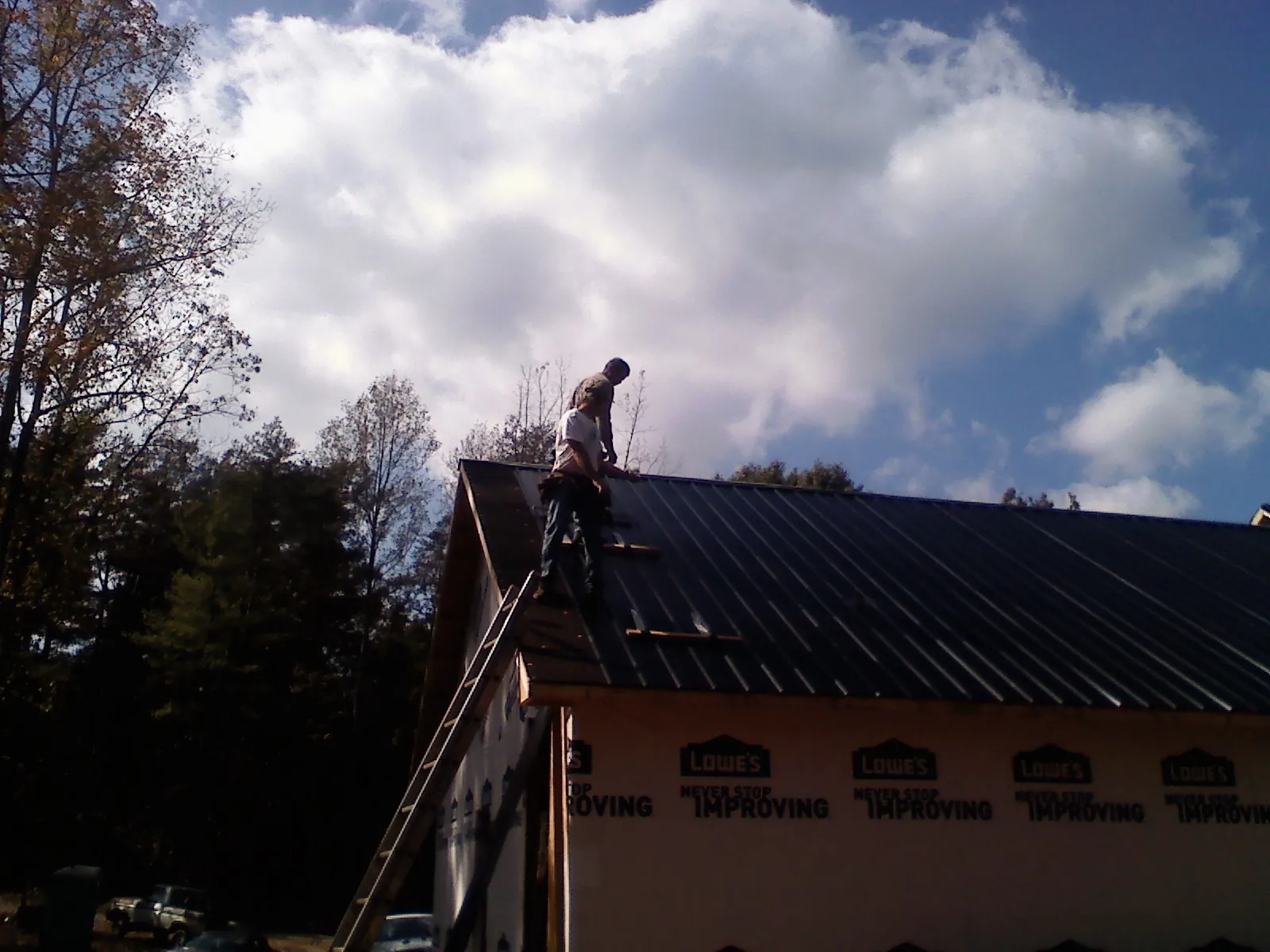 Roofer fastening dark metal panels high against a cloudy sky, from a Roof Inspection job in Tuxedo Park