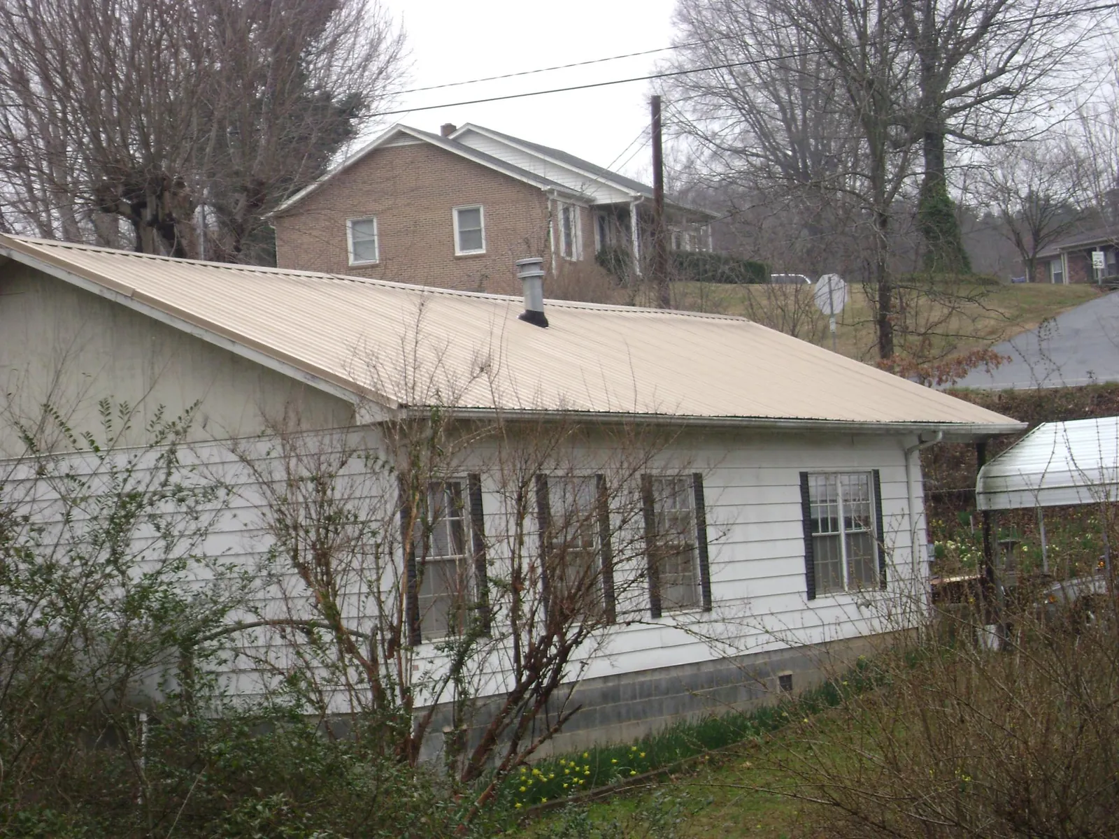 Tan metal roof on a white sided house set into a hillside — Commercial Roofing by Roofing Brothers in Tuxedo Park