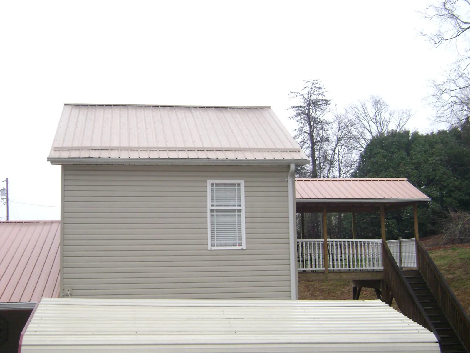 Tan metal roofs on a two story addition and attached porch, from a Roof Replacement job in Tuxedo Park