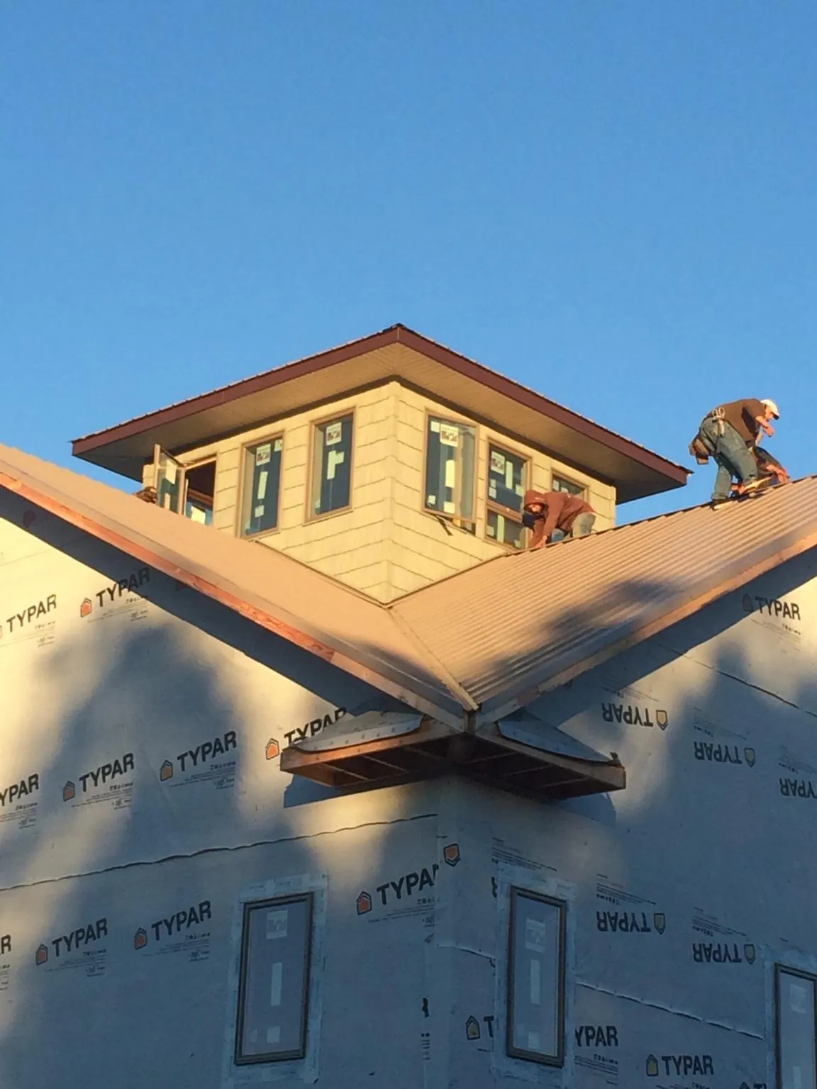 Roofers working around a rooftop cupola on a new metal roof at sunset — Roof Waterproofing in Tuxedo Park by Roofing Brothers